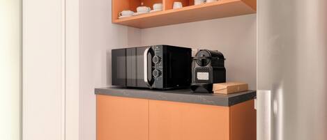 A kitchen with a microwave, coffee maker, and a shelf with cups and plates.
