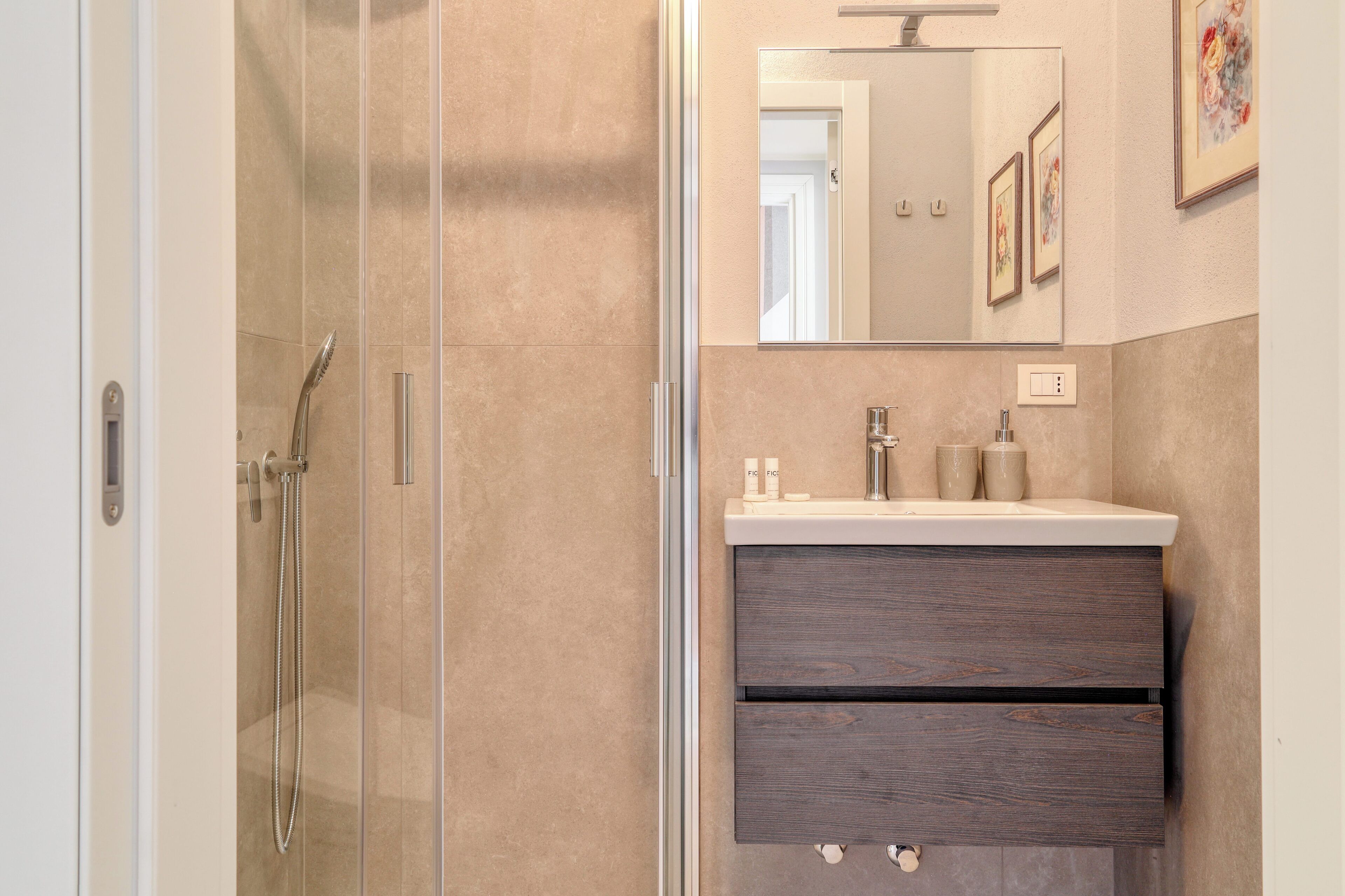 A modern bathroom with a glass-enclosed shower, a vanity with a dark wood drawer, and a mirror above the sink.