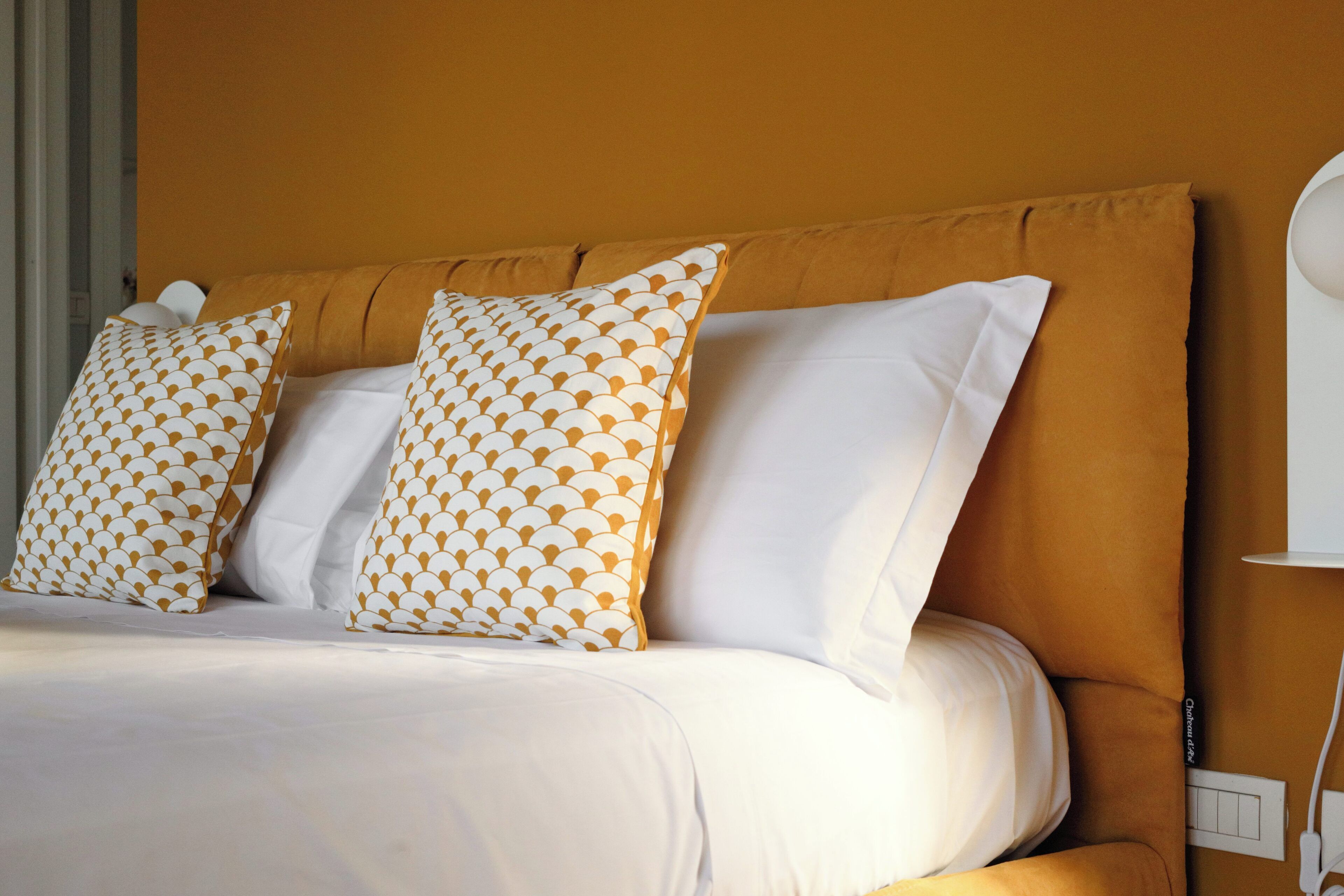 A bed with white and patterned pillows, a headboard, and a bedside table with a lamp.
