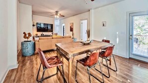 A modern living room with a wooden dining table, leather chairs, a sofa, and a ceiling fan.
