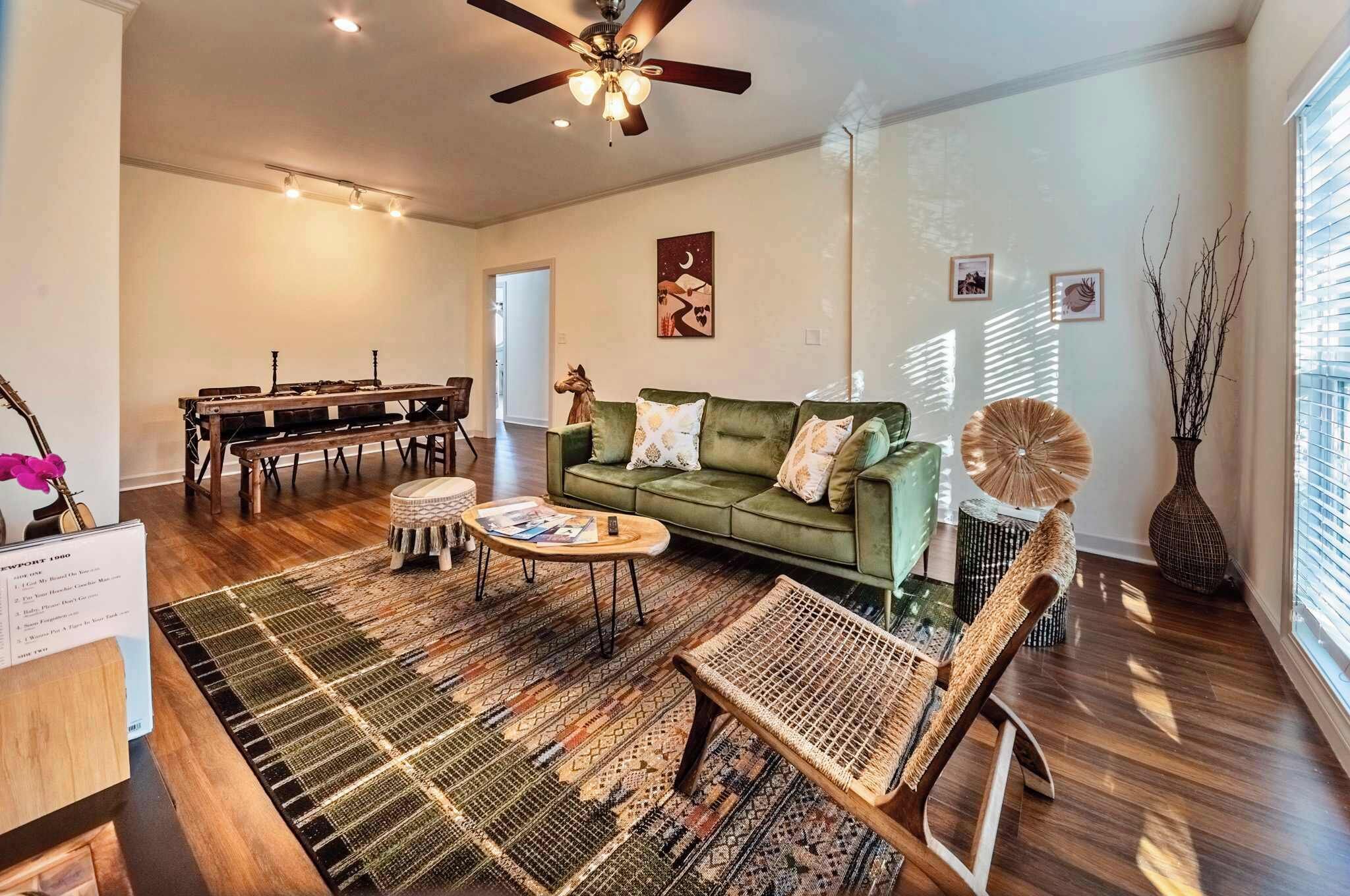 A spacious living room with a green sofa, a coffee table, and a dining area with a wooden table and chairs.