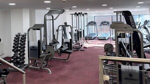 Una palestra con diverse attrezzature per esercizi, tapis roulant e un pavimento ricoperto di tappeto rosso.