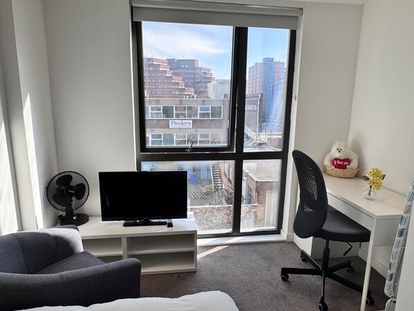 Una habitación de hotel moderna con un ventanal grande, un televisor de pantalla plana, un escritorio, una silla y una cama.