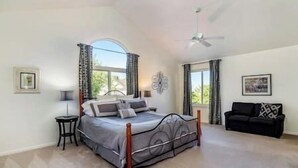A spacious bedroom with a large bed, a ceiling fan, and a view of the outdoors through a window.