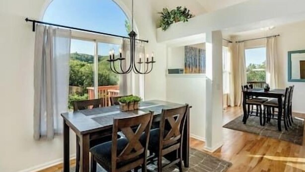 A dining area with a table and chairs, a chandelier, and a view of greenery outside.