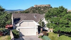 A residential house with a garage, surrounded by greenery and a hill with a fort-like structure in the background.