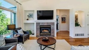 A spacious living room with a fireplace, a flat-screen TV mounted above it, and a comfortable seating area with a sofa and a coffee table.