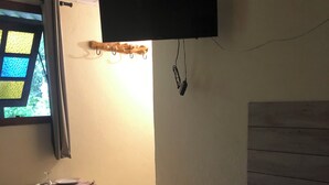 A bedroom with a bed, a small table, a window with curtains, a wall-mounted TV, and a wooden headboard. - Recanto Mineiro (São Lourenço)