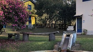 A small outdoor water feature with a circular basin and two slides, surrounded by grass and a few trees. - Recanto Mineiro (São Lourenço)