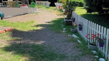 Een grindpad leidt naar een wit hek met pionnen, omgeven door groen en bloempotten.