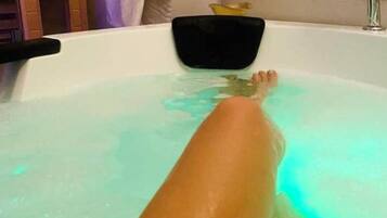 A bathtub with a person submerged in it, a black object on the edge, and a towel hanging on the wall.