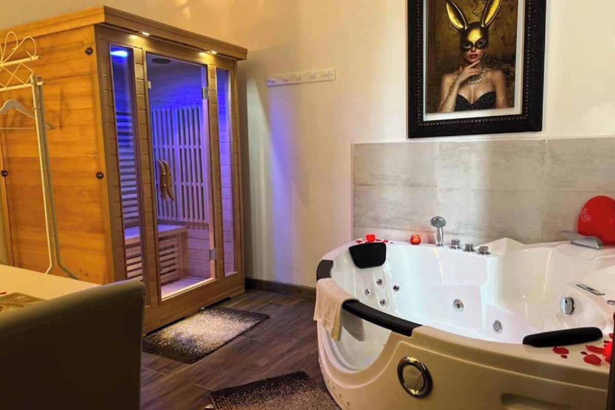 A modern bathroom with a large bathtub, wooden sauna, and a framed artwork on the wall.