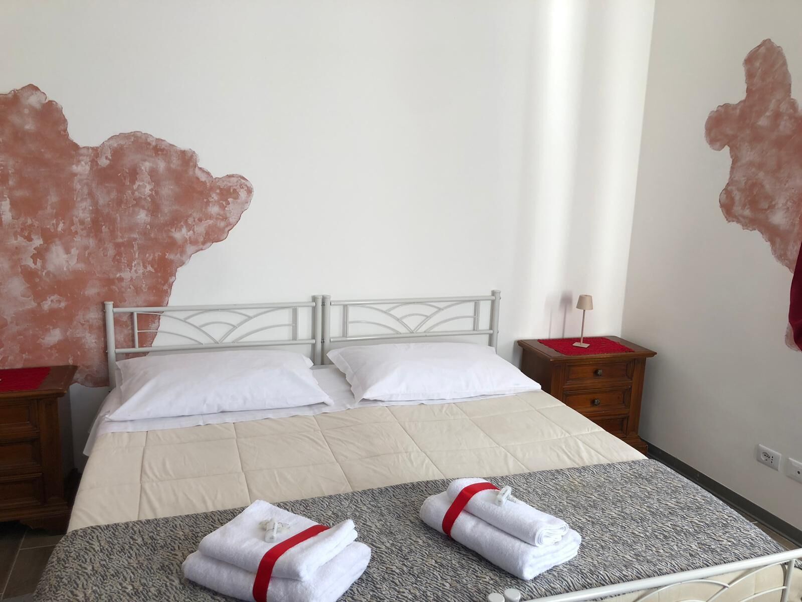 Habitación de hotel con cama, dos almohadas, mesita de noche con lámpara y perchero con toallas.