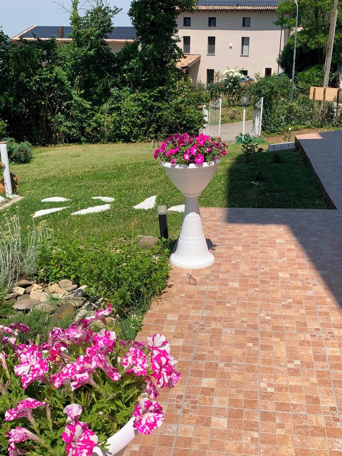 A garden pathway with a white flower pot, a tiled patio, and a building in the background.