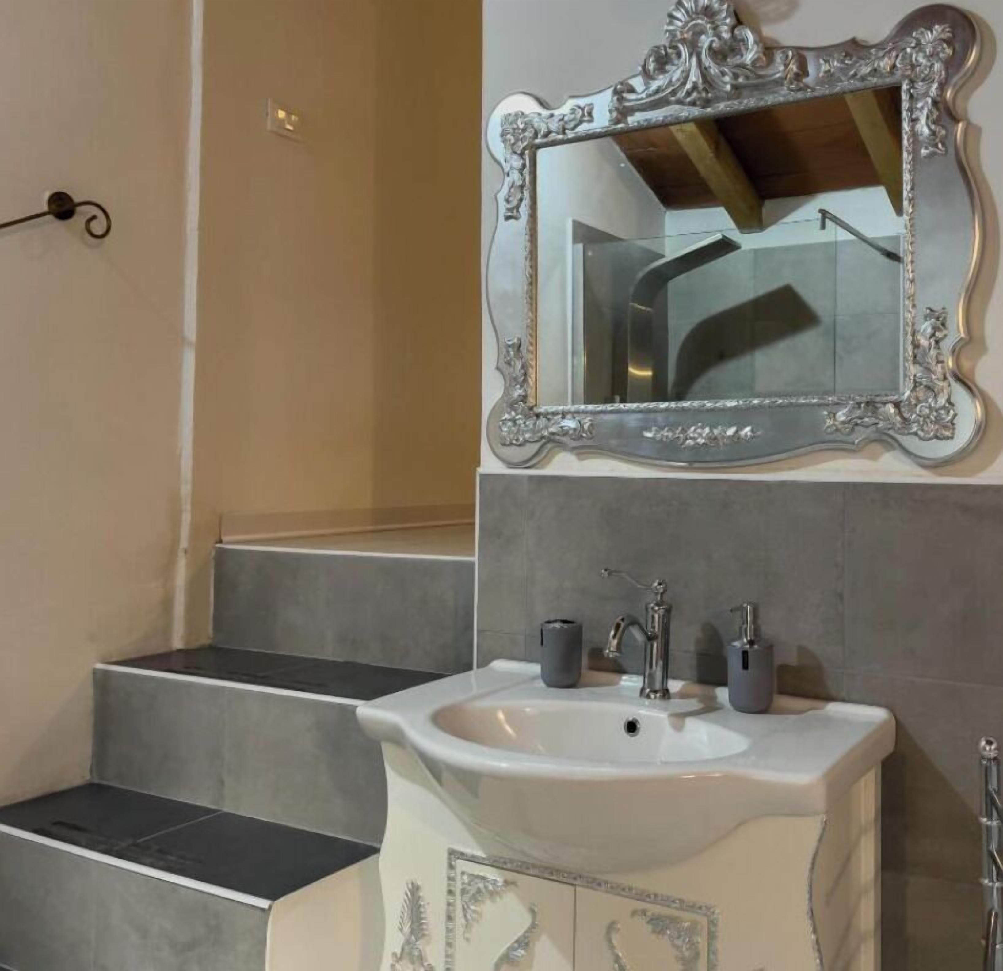 A bathroom with a white sink, two faucets, and a large ornate mirror.