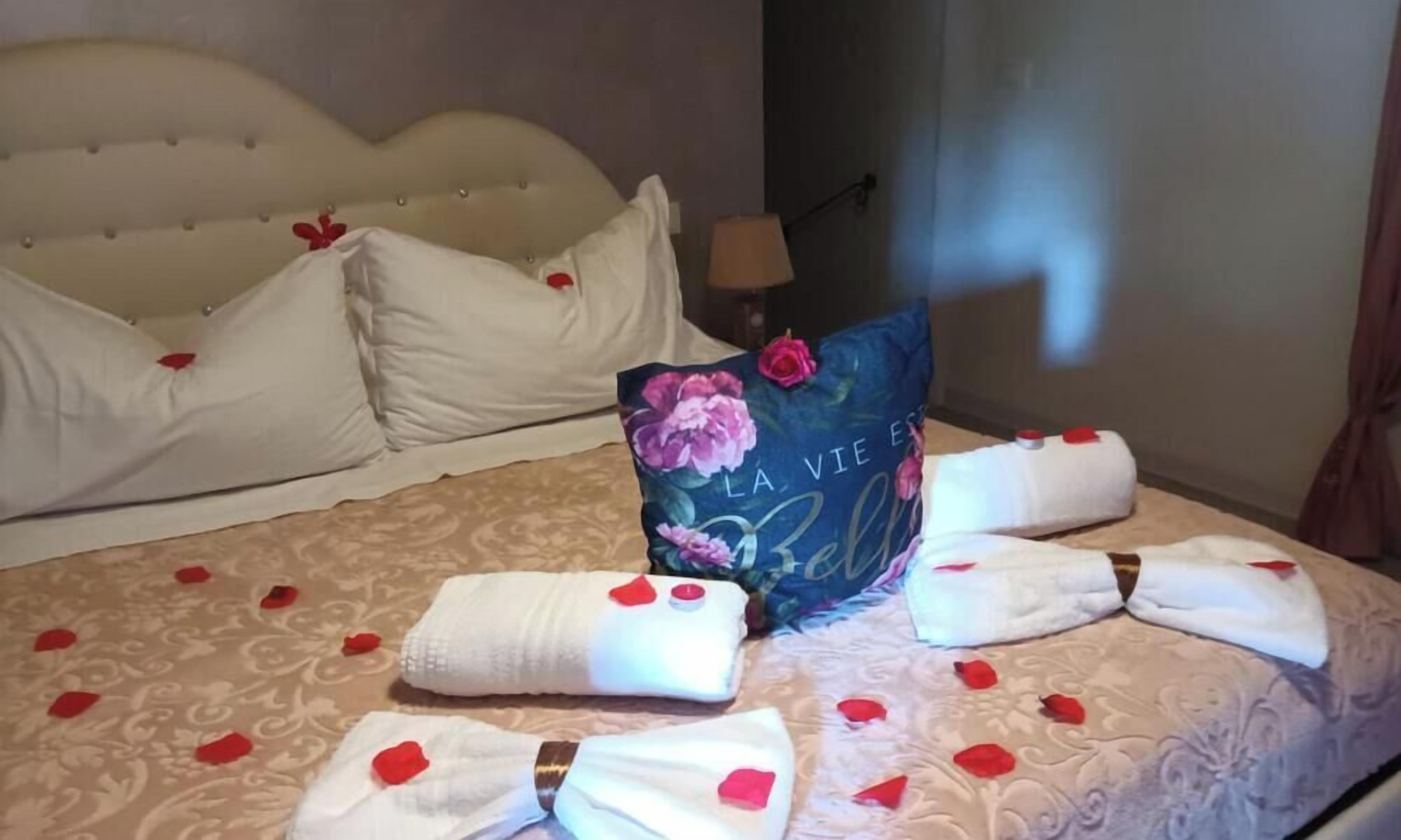 A bed with a floral pillow, a decorative pillow, and towels with rose petals.