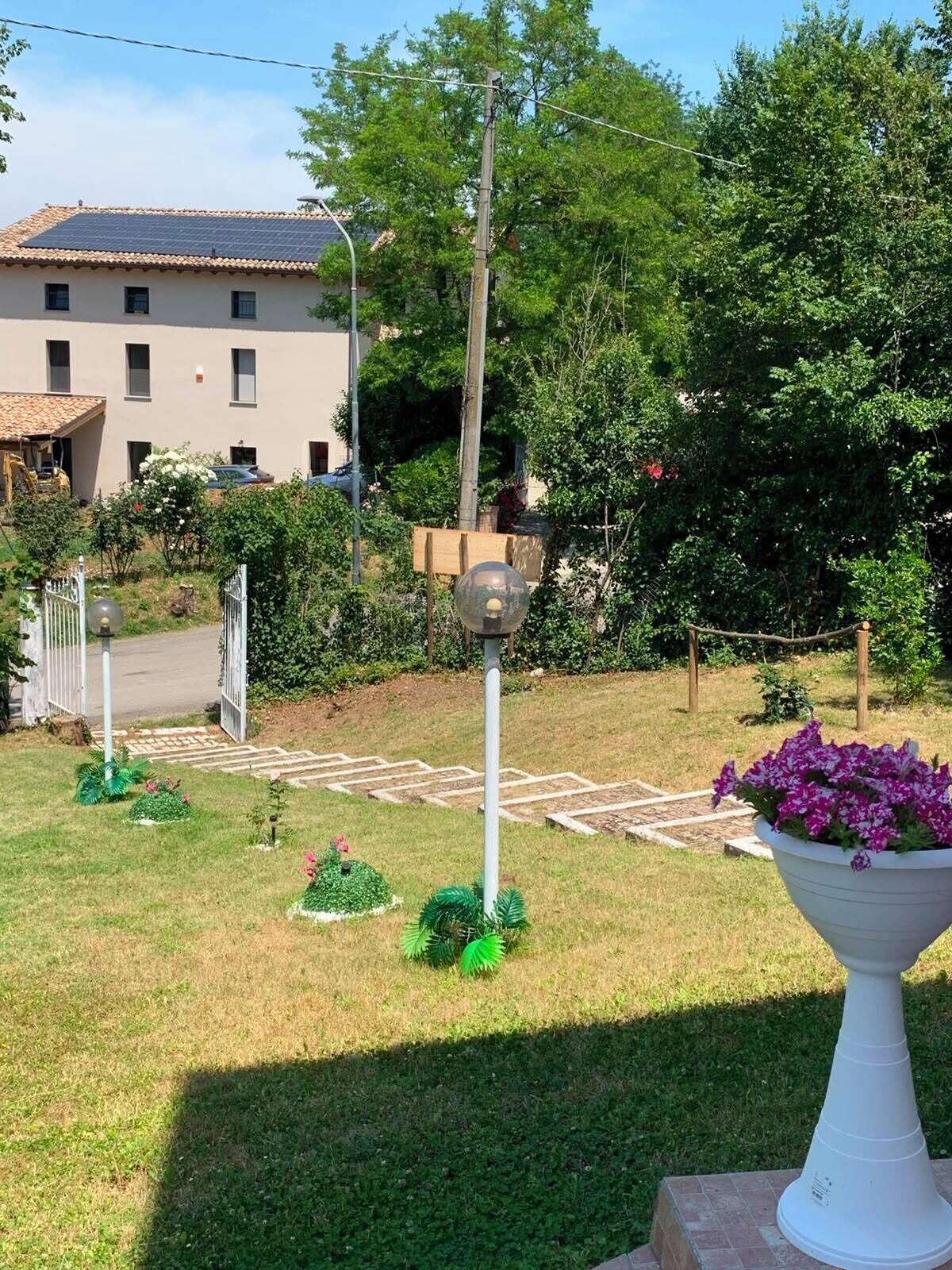 Zona residencial con una casa, un jardín y un objeto esférico, además de una maceta blanca.
