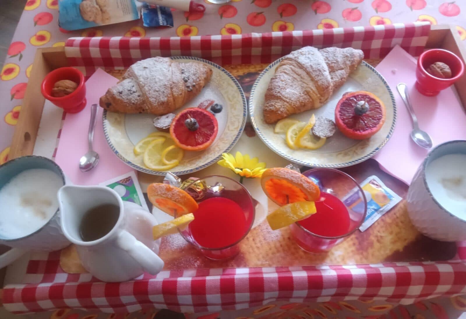 Bandeja de desayuno con croissants, rebanadas de fruta y bebidas sobre un mantel a cuadros.