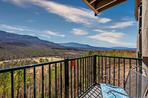 A balcony with a metal railing, a chair, and a view of mountains and a valley.