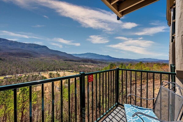 A balcony with a metal railing, a chair, and a view of mountains and a valley.