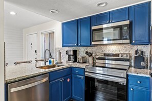 A modern kitchen with blue cabinets, stainless steel appliances, and granite countertops.