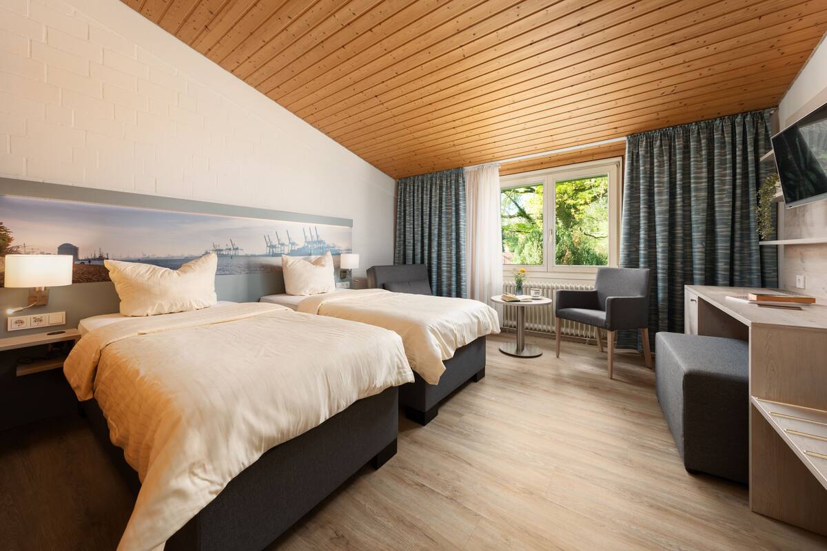 Ein Hotelzimmer mit zwei Betten, einem Schreibtisch, einem Stuhl und einem Vorhangfenster.