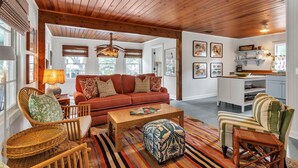 A spacious living room with a wooden ceiling, a red sofa, wicker chairs, and a striped rug. - Byrd Shack - Walk to Edisto Beach! (Edisto Island)