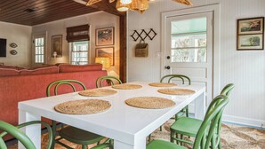 A dining area with a white table and green chairs, surrounded by a red couch and a wooden ceiling. - Byrd Shack - Walk to Edisto Beach! (Edisto Island)