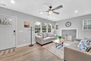 A modern living room with a sofa, coffee table, and a fireplace. - Charming 3BR Home, fenced yard, BBQ, mini golf, yard games--minutes to uptown (Charlotte)