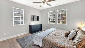 Quarto com cama, ventilador de teto, cômoda e duas janelas.
