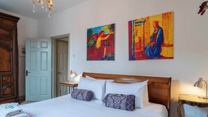 Ein ordentlich bezogenes Bett mit weißen Leinentüchern und gemusterten Kissen, ein hölzerner Kopfseitenverkleidung und zwei Bilder an der Wand.