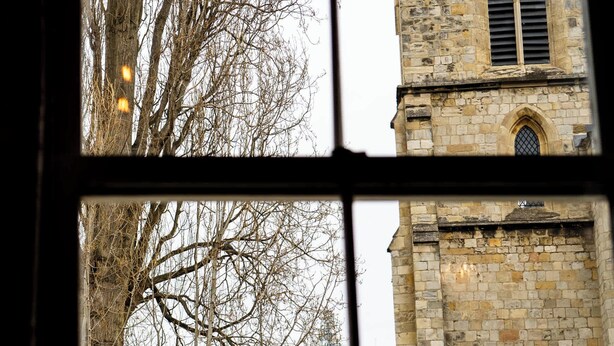 Blick aus dem Fenster auf ein Steinhaus mit einem Turm und Rundbogenfenstern.