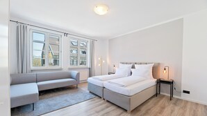 A modern hotel room with a large bed, a sofa, and a view of buildings outside the window. - Steiners Hotel (Stuttgart)