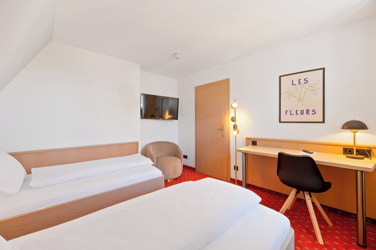 A hotel room with two beds, a desk, a chair, a TV, and a framed picture on the wall.
