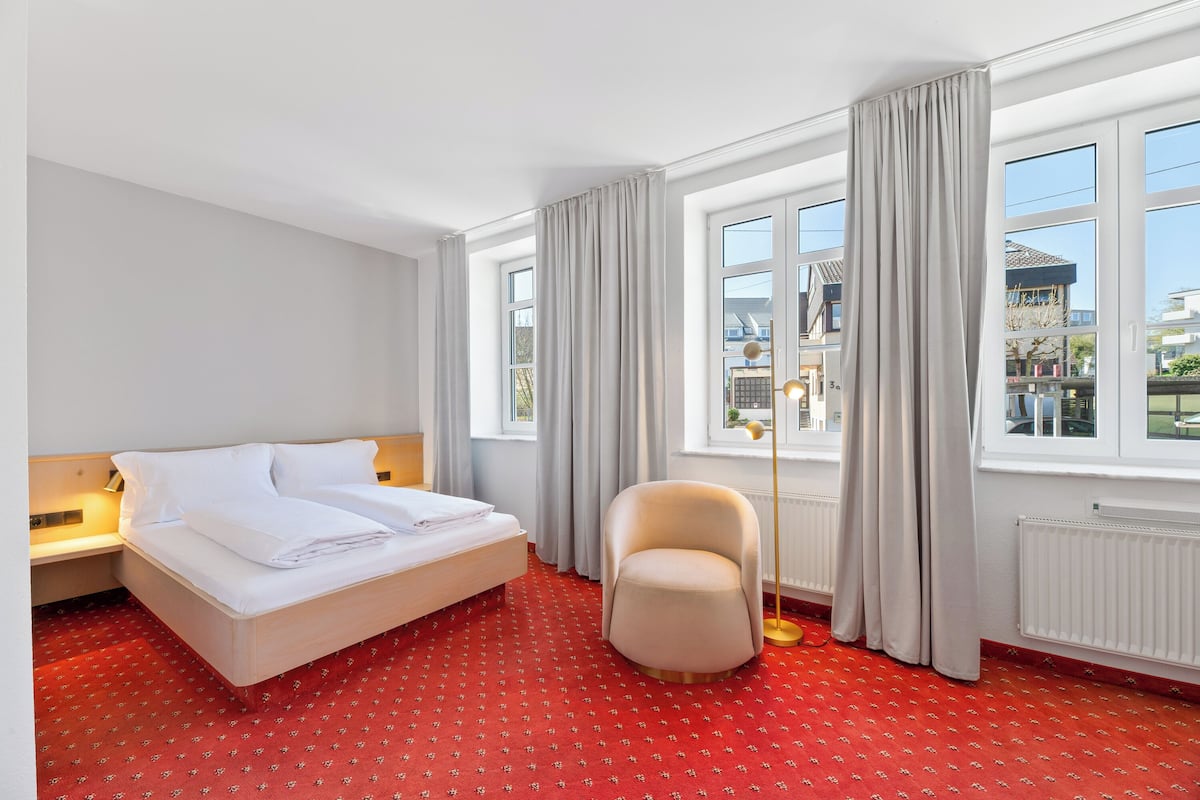 A hotel room with a bed, a chair, a window, and a radiator.