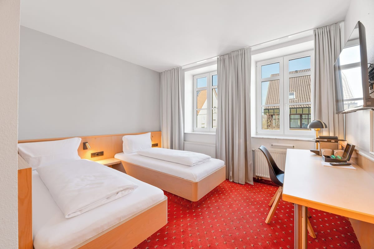 A hotel room with two beds, a desk, and a window with curtains.