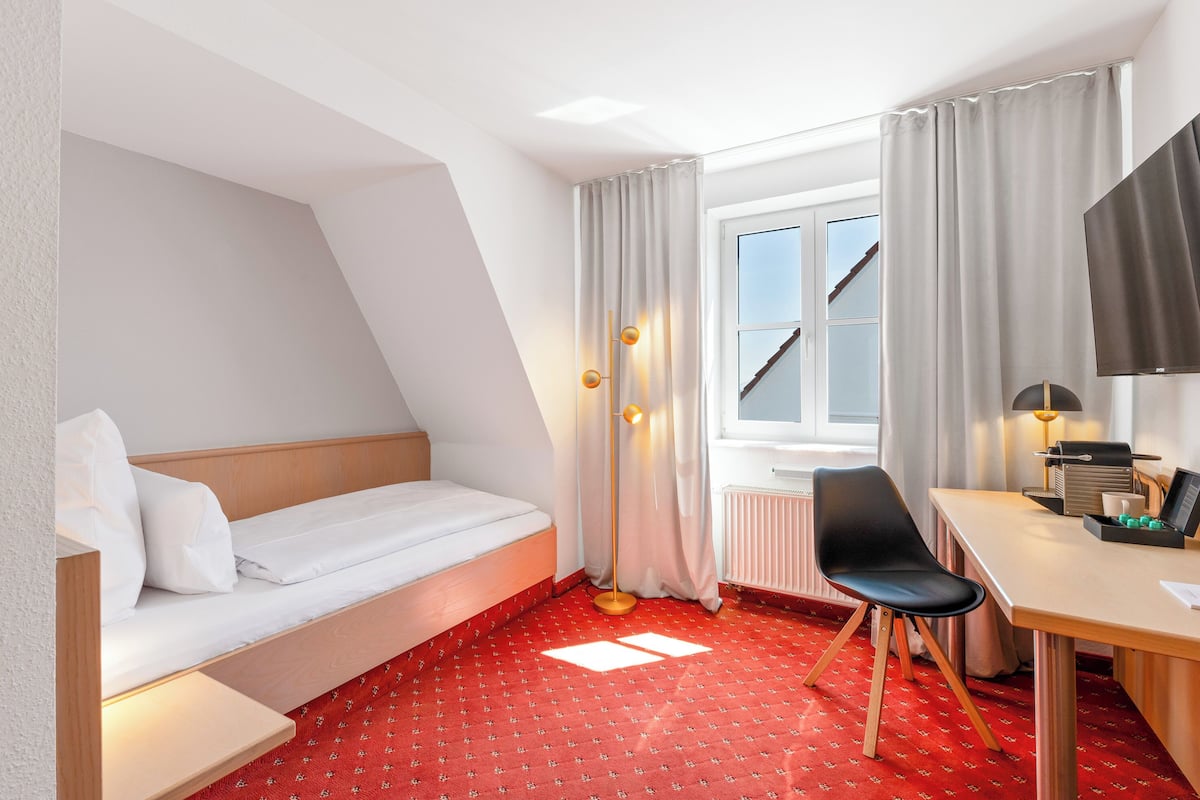A hotel room with a bed, a desk, a chair, a TV, and a window with curtains.