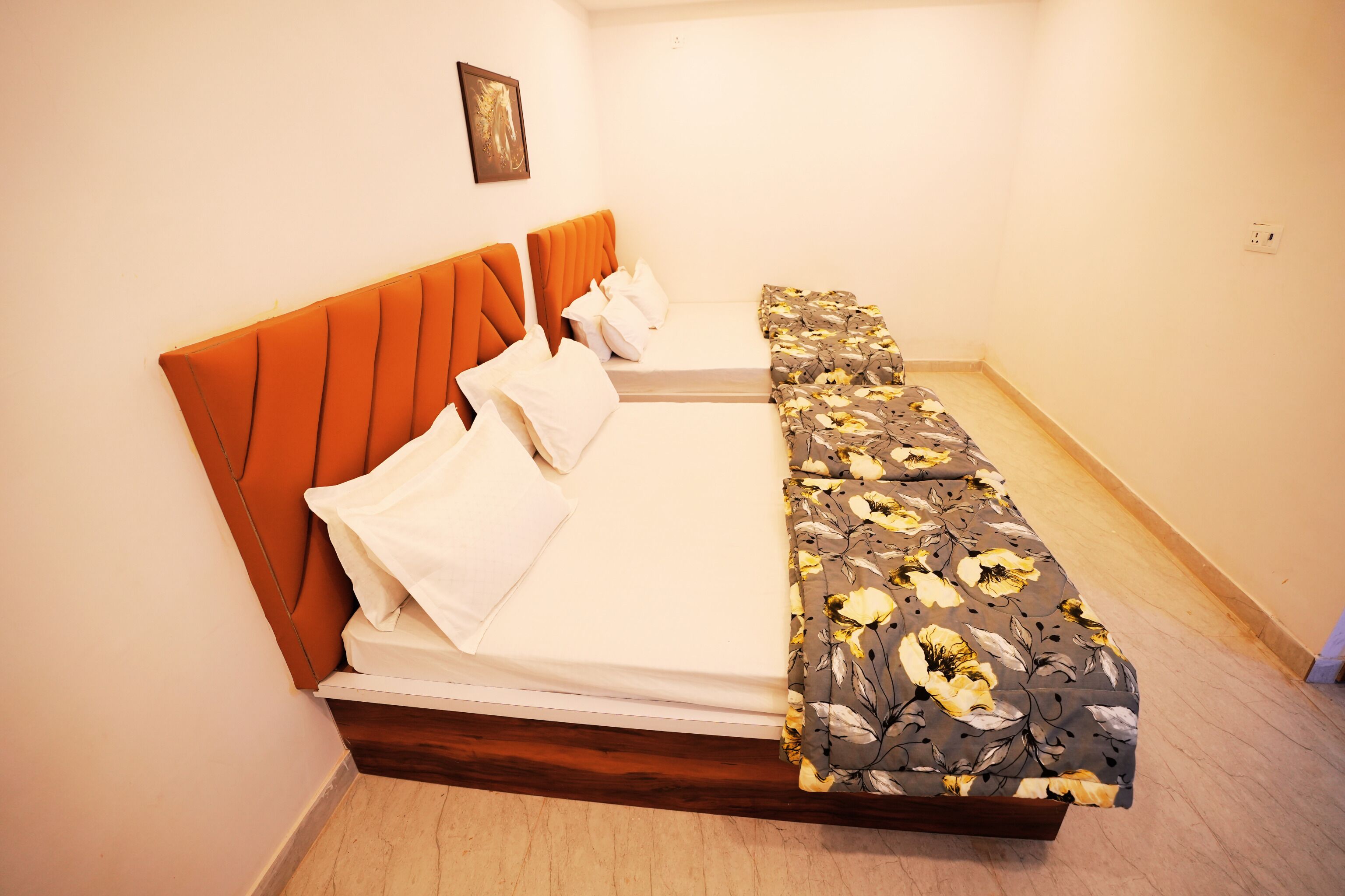 Uma cama de solteiro com cabeceira laranja e colcha estampada em um quarto com paredes brancas e piso de madeira.