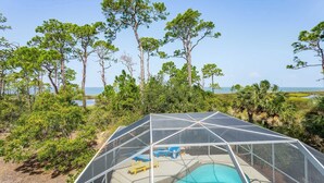 Un espace piscine doté d’une structure couverte, entouré d’arbres et offrant une vue sur l’océan.