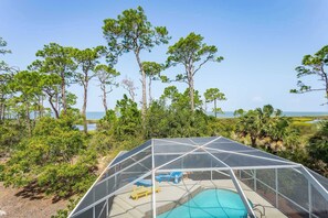 Zona de piscina con estructura cubierta, rodeada de árboles y vista al océano.