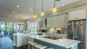 Une cuisine spacieuse dotée d’un îlot central, de meubles blancs, d’appareils électroménagers en acier inoxydable et de luminaires suspendus.
