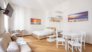 Een moderne, goed verlichte slaapkamer met een houten vloer, een bed, een bureau met stoel, een eettafel met stoelen, en twee wanddecoraties.