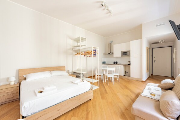 A modern hotel room with a wooden bed, a white sofa, a kitchenette, and a separate dining area. - Cozy flat in historical centre of Genova (Genoa)
