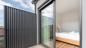 A modern bedroom with a sliding glass door, a bed with white bedding, and a view of the cityscape.