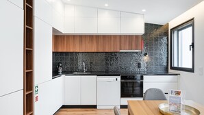 A modern kitchen with white cabinets, a wooden upper shelf, a black backsplash, and a window with a view.