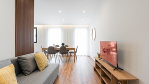 A modern living room with a grey sofa, wooden floor, and a flat-screen TV on a wooden stand.