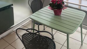A balcony with a green table and chairs, a potted plant, and a view of buildings and trees. - Le square Spacious apartment with terrace & garage, quiet location near Colmar  (Sundhoffen)
