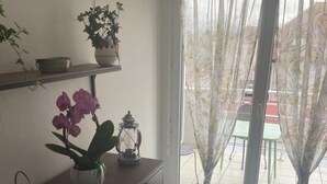 A room with a wooden cabinet, a potted plant, a lantern, and a view through a glass door. - Le square Spacious apartment with terrace & garage, quiet location near Colmar  (Sundhoffen)