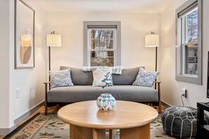 A cozy living room with a grey sofa, patterned cushions, a round wooden coffee table, and two floor lamps.