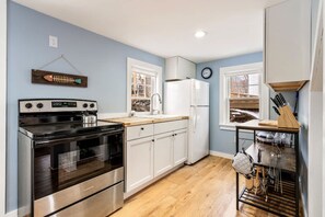 A compact kitchen with a stainless steel stove, white cabinets, a sink, and a window with a view of the outside.